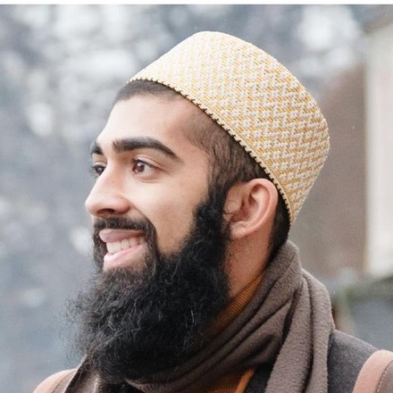Taher Lokhandwala, smiling, wearing a gold topi in front of snowy mountains